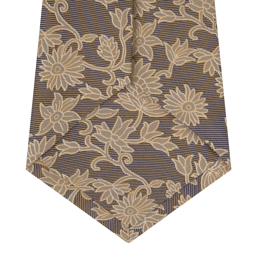 The Copper Floral Occasion Silk Tie by Turnbull & Asser features a gold floral jacquard pattern on brown silk, elegantly rolled on a white surface—an ideal choice for weddings.