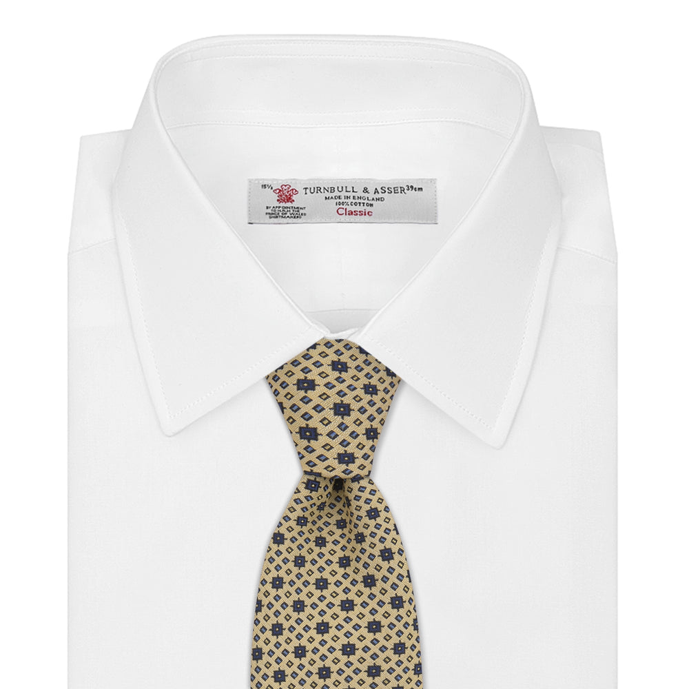 The Turnbull & Asser Pale Yellow Geometric Silk Tie features a subtle navy blue floral pattern and is displayed rolled on a white background.