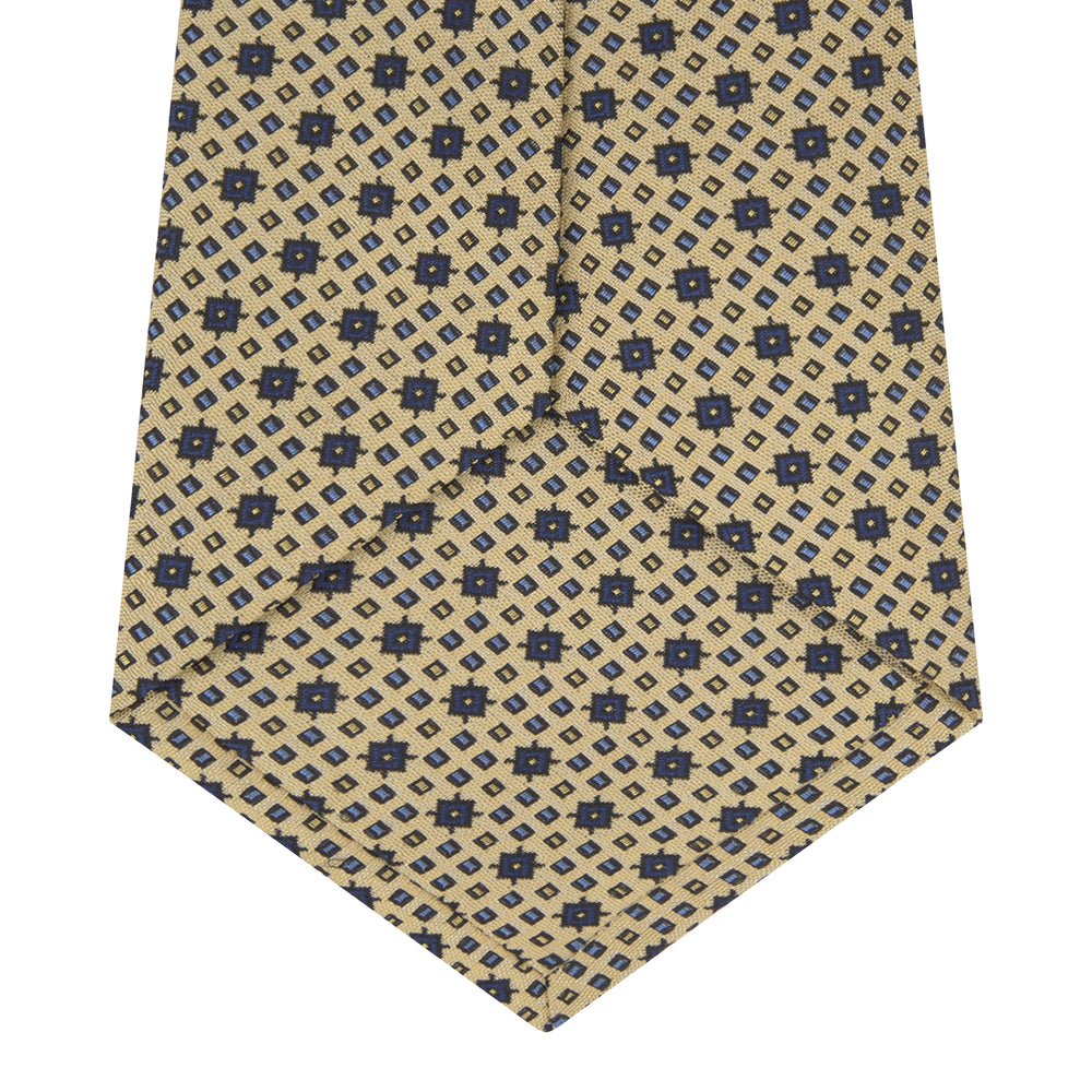 The Turnbull & Asser Pale Yellow Geometric Silk Tie features a subtle navy blue floral pattern and is displayed rolled on a white background.