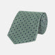 The Leaf Green Geometric Silk Tie by Turnbull & Asser features a repeating pattern of small navy blue and white floral shapes, evoking a mid-century motif. It is neatly rolled and displayed on a white background.