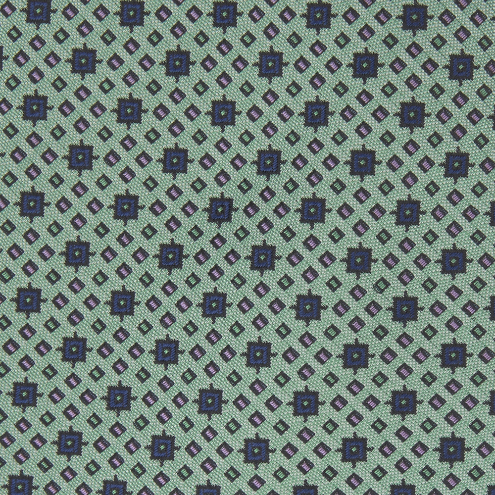 The Leaf Green Geometric Silk Tie by Turnbull & Asser features a repeating pattern of small navy blue and white floral shapes, evoking a mid-century motif. It is neatly rolled and displayed on a white background.