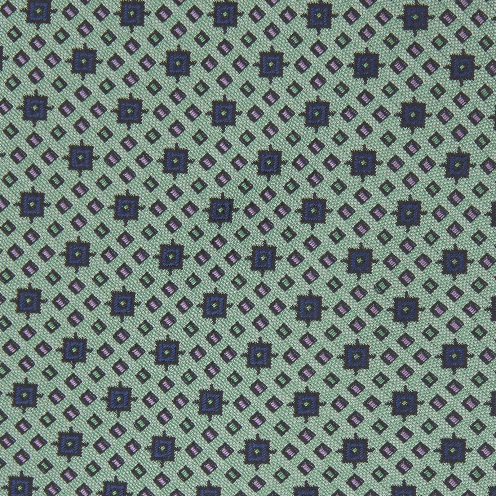 View 3 of product The Leaf Green Geometric Silk Tie by Turnbull & Asser features a repeating pattern of small navy blue and white floral shapes, evoking a mid-century motif. It is neatly rolled and displayed on a white background.