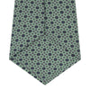 View 4 of product The Leaf Green Geometric Silk Tie by Turnbull & Asser features a repeating pattern of small navy blue and white floral shapes, evoking a mid-century motif. It is neatly rolled and displayed on a white background.