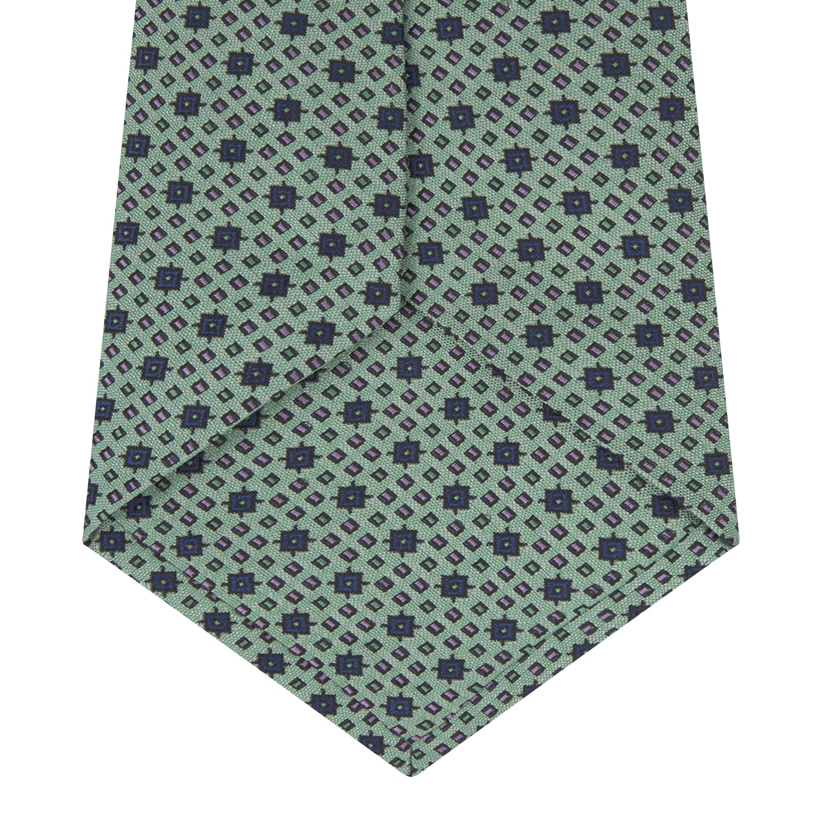 View 4 of product The Leaf Green Geometric Silk Tie by Turnbull & Asser features a repeating pattern of small navy blue and white floral shapes, evoking a mid-century motif. It is neatly rolled and displayed on a white background.