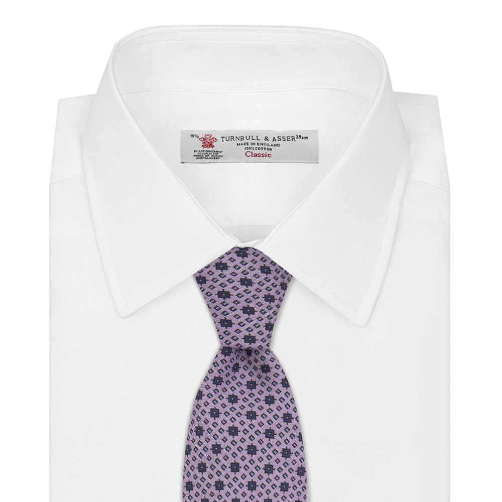 The Turnbull & Asser Lilac Geometric Silk Tie features a small, repeating mid-century motif in dark purple and black on white—an ideal accent for tailored jackets.