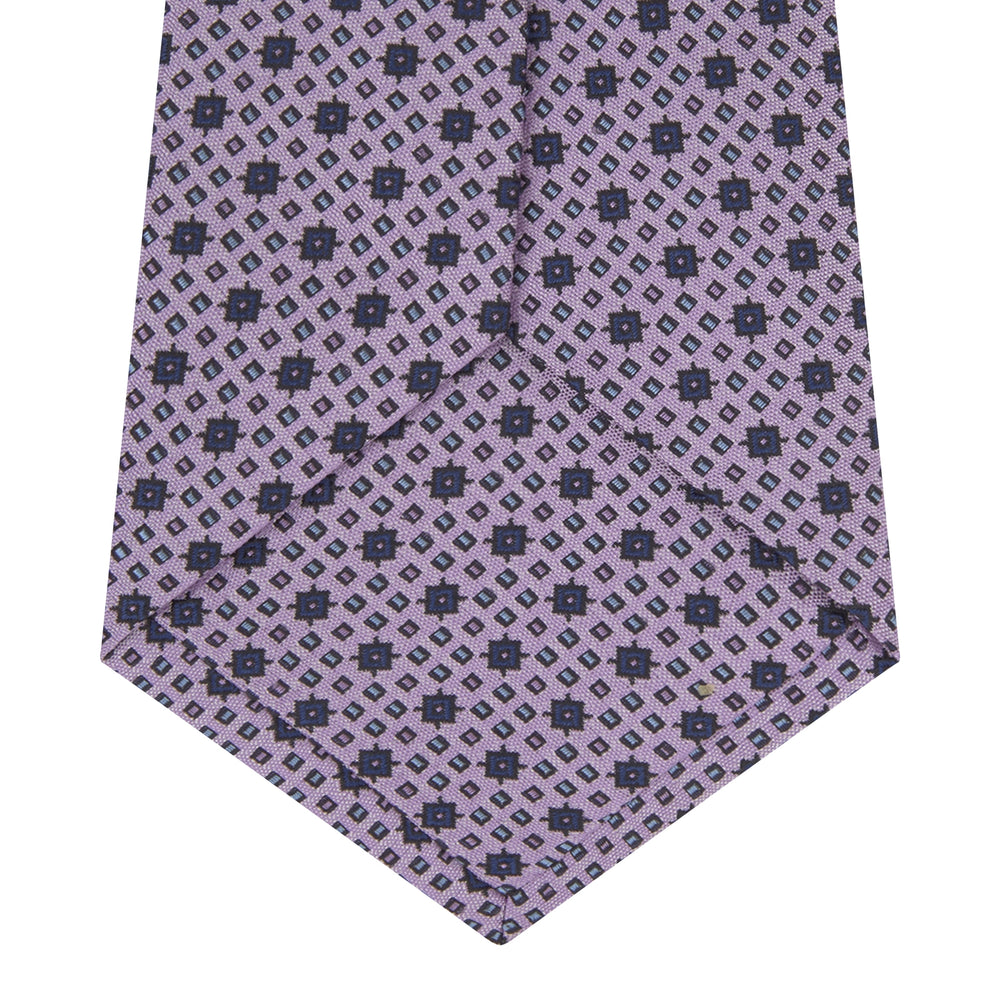 The Turnbull & Asser Lilac Geometric Silk Tie features a small, repeating mid-century motif in dark purple and black on white—an ideal accent for tailored jackets.