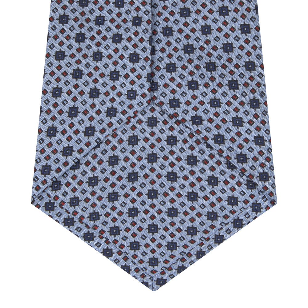 The Turnbull & Asser Sky Blue Geometric Silk Tie features a mid-century dark blue and maroon motif on light blue silk, shown against a white background—ideal for pairing with tailored jackets.