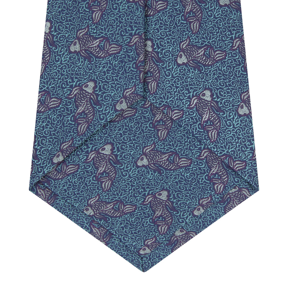 The Turnbull & Asser Turquoise Carp Silk Tie is woven in England, featuring a repeating white and brown carp design on a light blue background with intricate swirling patterns.