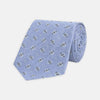View 1 of product The Turnbull & Asser Sky Blue Star Flowers Silk Tie features a small white and dark blue square and star flower pattern on jacquard silk, shown rolled up against a plain white background.