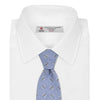 View 2 of product The Turnbull & Asser Sky Blue Star Flowers Silk Tie features a small white and dark blue square and star flower pattern on jacquard silk, shown rolled up against a plain white background.