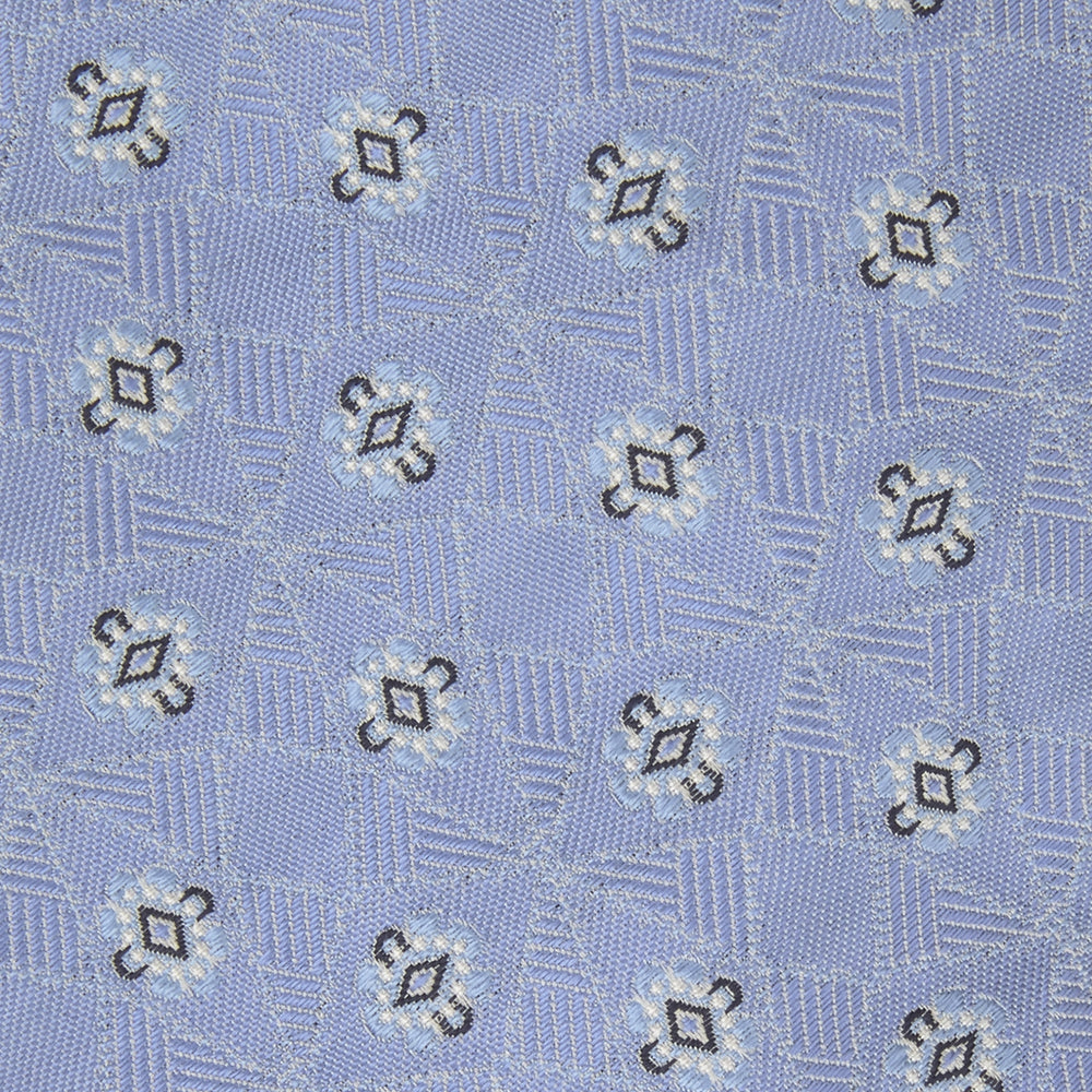 The Turnbull & Asser Sky Blue Star Flowers Silk Tie features a small white and dark blue square and star flower pattern on jacquard silk, shown rolled up against a plain white background.