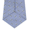 View 4 of product The Turnbull & Asser Sky Blue Star Flowers Silk Tie features a small white and dark blue square and star flower pattern on jacquard silk, shown rolled up against a plain white background.