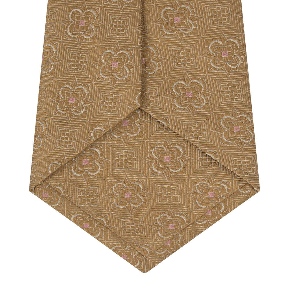 The Gold Flower Mosaic Silk Tie by Turnbull & Asser features an intricate gold jacquard pattern of geometric shapes and floral designs in pink and light brown hues.