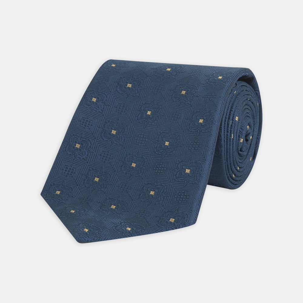 The Deep Turquoise Flower Mosaic Silk Tie by Turnbull & Asser features a jacquard design in blue with a subtle geometric pattern and small gold square accents evenly spaced across the fabric.