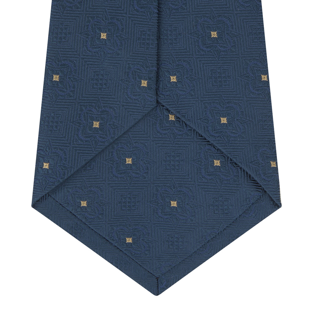 The Deep Turquoise Flower Mosaic Silk Tie by Turnbull & Asser features a jacquard design in blue with a subtle geometric pattern and small gold square accents evenly spaced across the fabric.