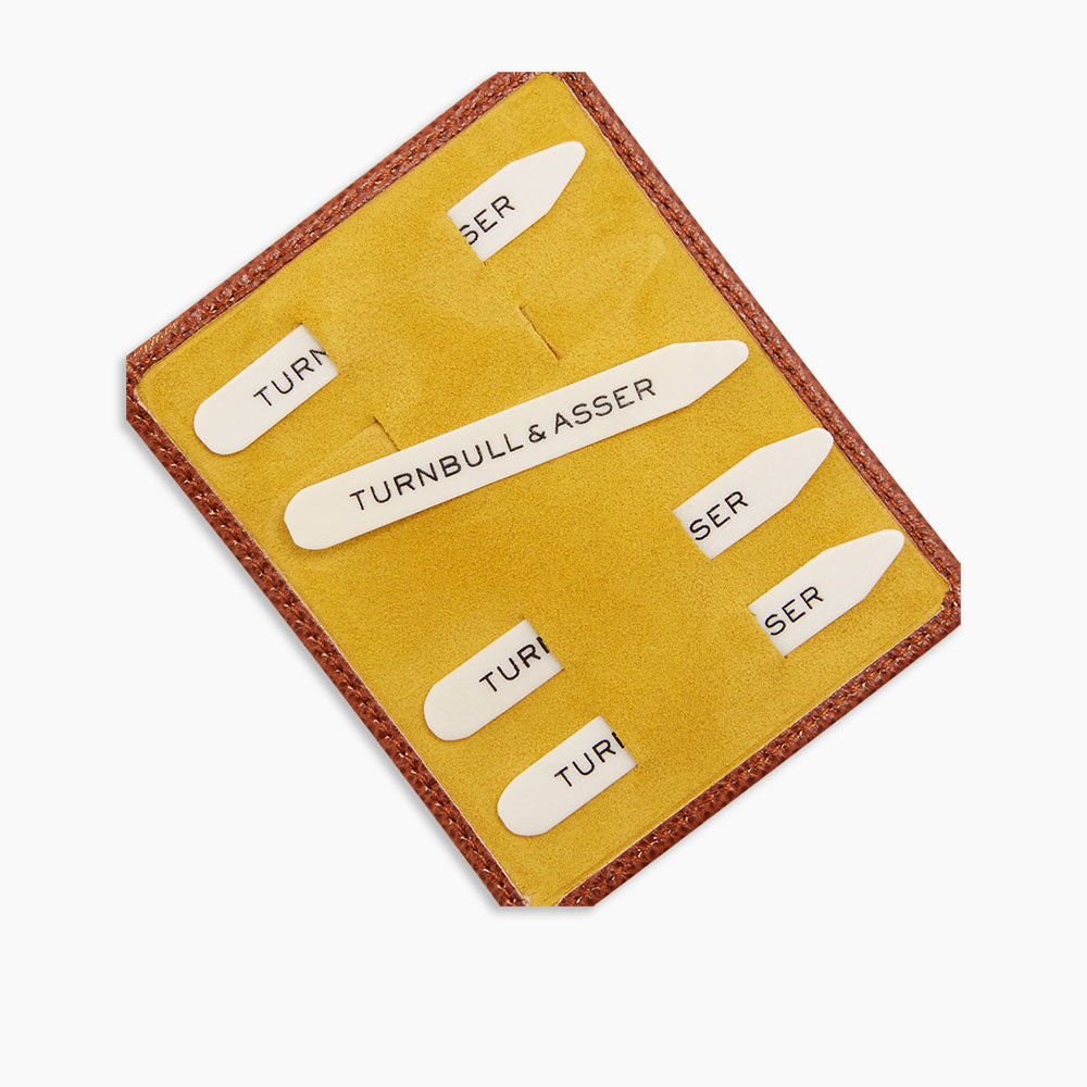 Turnbull & Asser’s Bone Collar Stays in a tan leather, mustard suede-lined tray include six white bone stays—each labeled—offering refined style and perfectly crisp collars.