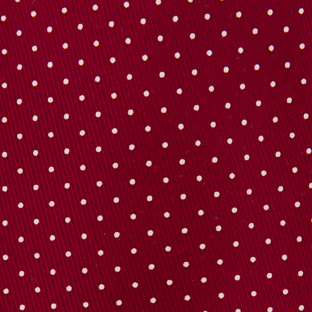 The Turnbull & Asser Burgundy and White Small Spot Printed Silk Tie, shown rolled against a plain white background, is an elegant accessory ideal for the office.