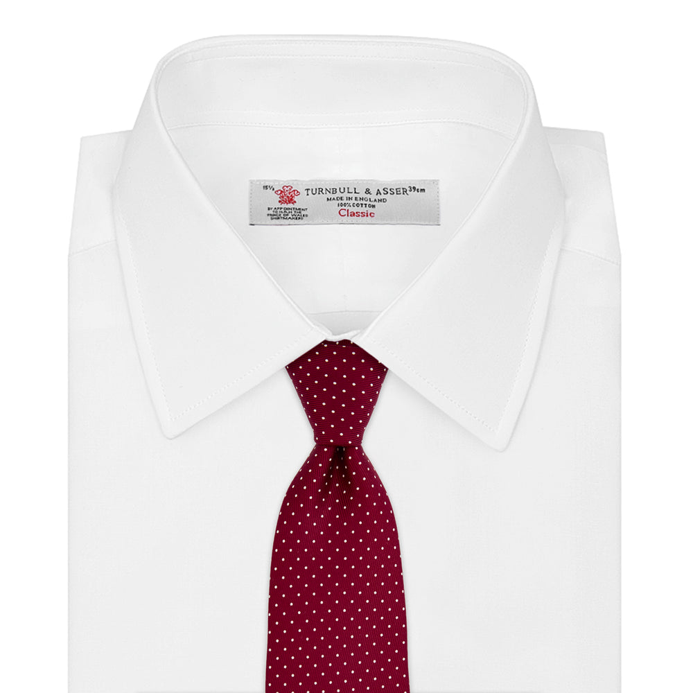 The Turnbull & Asser Burgundy and White Small Spot Printed Silk Tie, shown rolled against a plain white background, is an elegant accessory ideal for the office.