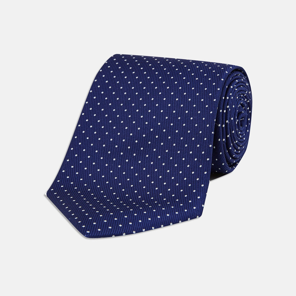The Blue and White Small Spot Printed Silk Tie by Turnbull & Asser, shown rolled on a white background, features a refined white polka dot pattern—ideal for complementing any office shirt.