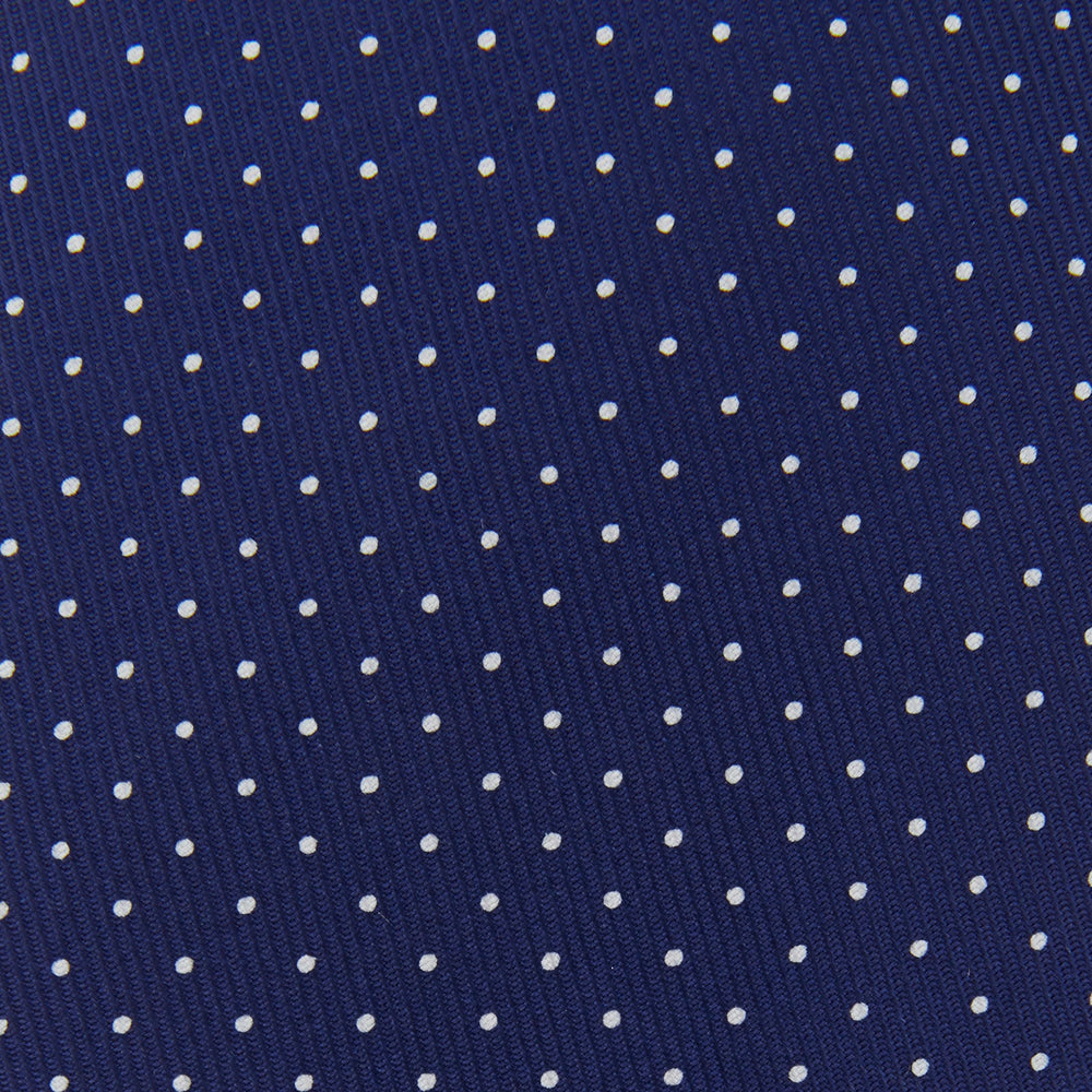 The Blue and White Small Spot Printed Silk Tie by Turnbull & Asser, shown rolled on a white background, features a refined white polka dot pattern—ideal for complementing any office shirt.