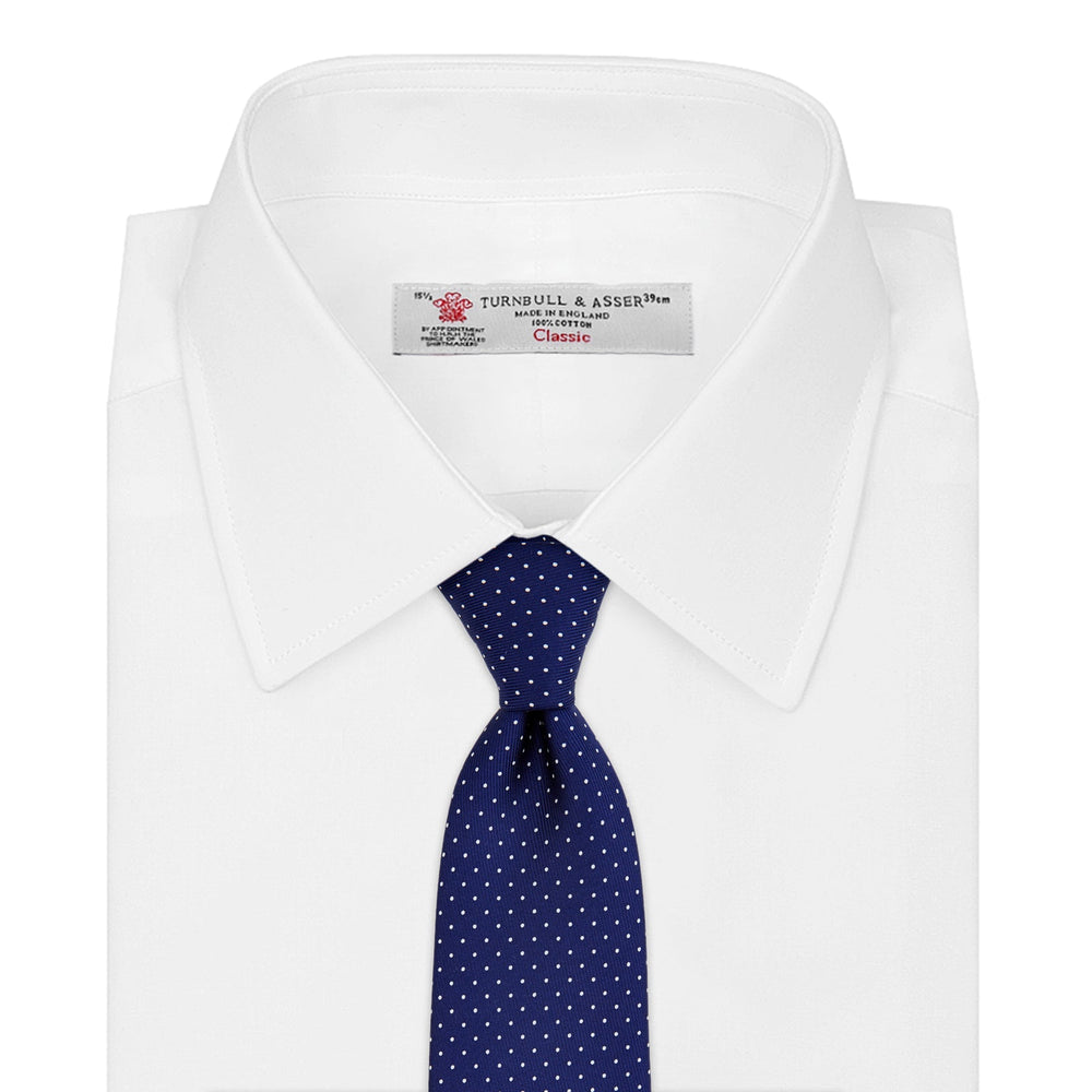 The Blue and White Small Spot Printed Silk Tie by Turnbull & Asser, shown rolled on a white background, features a refined white polka dot pattern—ideal for complementing any office shirt.