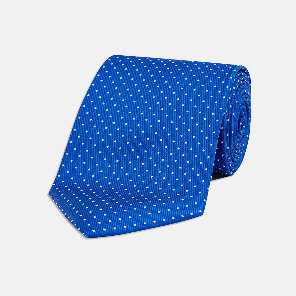 The Turnbull & Asser Royal Blue and White Small Spot Printed Silk Tie, shown rolled on a white background, features a refined spot pattern—ideal for complementing your office shirt.