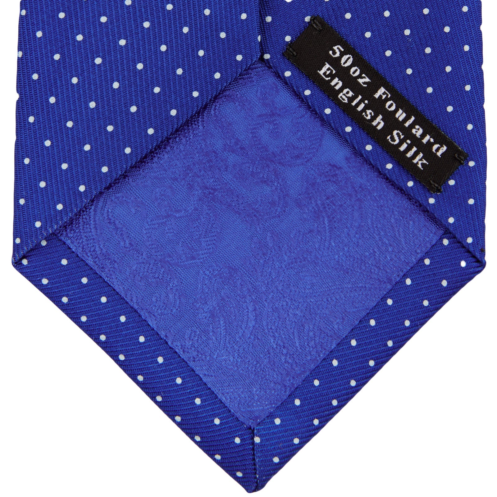View 4 of product The Turnbull & Asser Slim Royal Blue and White Small Spot Printed Silk Tie, featuring white polka dots, is ideal for office wear and shown rolled up on a plain white background.