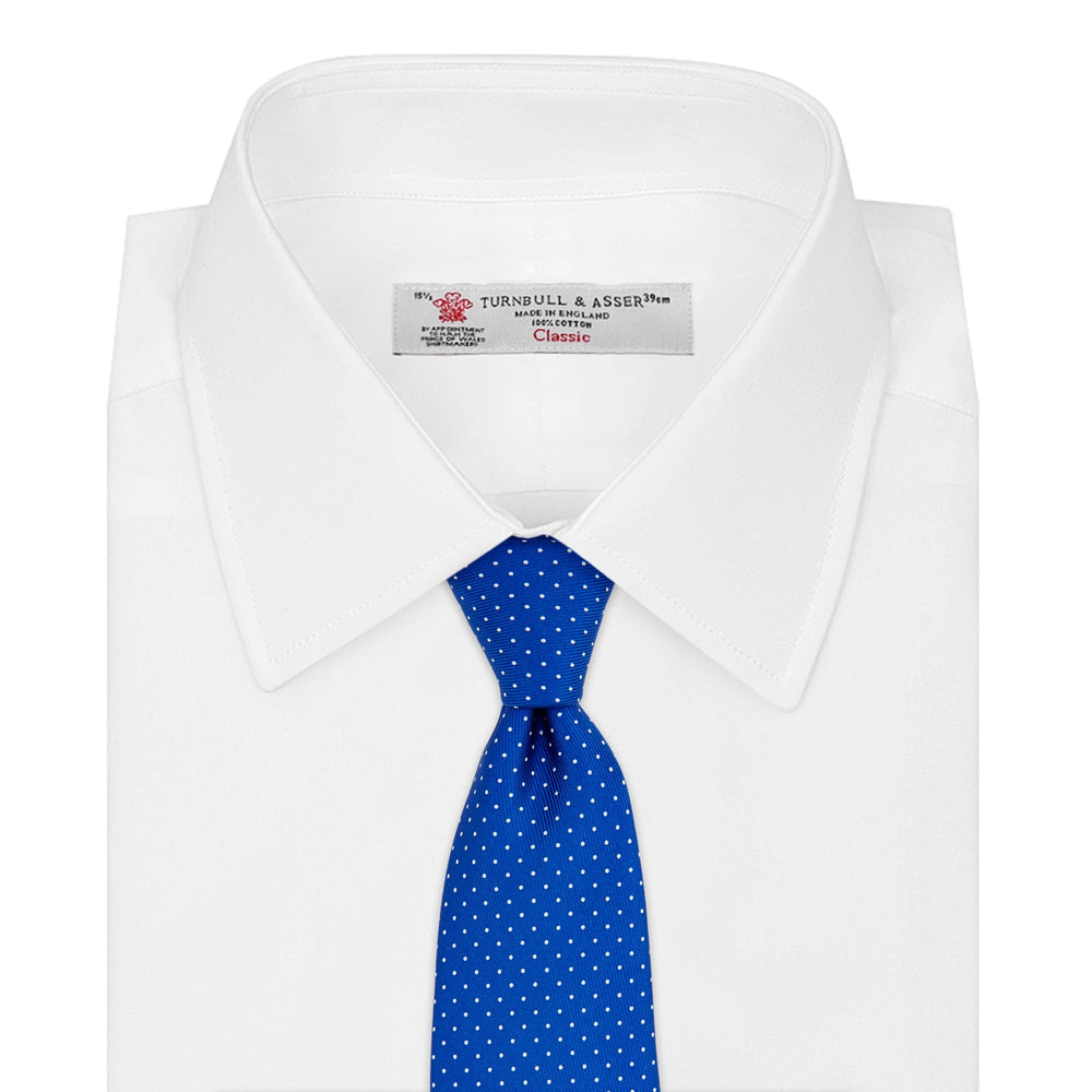 The Turnbull & Asser Royal Blue and White Small Spot Printed Silk Tie, shown rolled on a white background, features a refined spot pattern—ideal for complementing your office shirt.