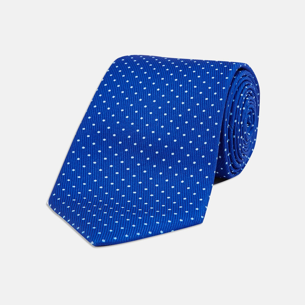 The Turnbull & Asser Slim Royal Blue and White Small Spot Printed Silk Tie, featuring white polka dots, is ideal for office wear and shown rolled up on a plain white background.
