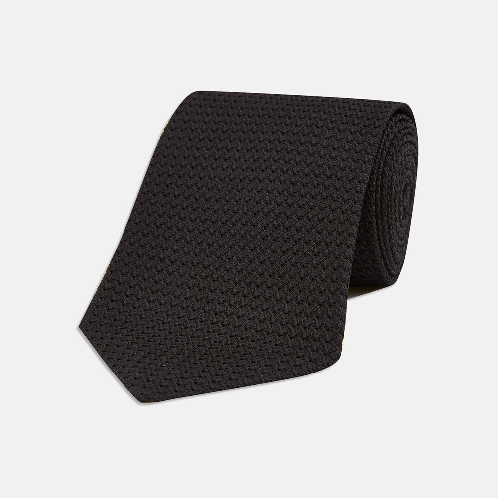 The Turnbull & Asser Long Black Grenadine Silk Tie features a subtle woven pattern and knitted appearance, shown rolled at one end against a plain white background.
