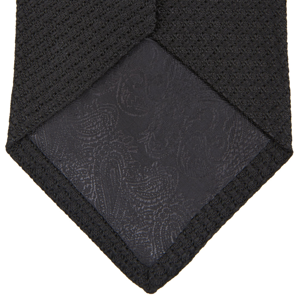 The Turnbull & Asser Long Black Grenadine Silk Tie features a subtle woven pattern and knitted appearance, shown rolled at one end against a plain white background.