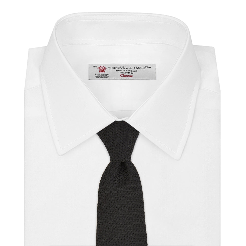 The Slim Black Grenadine Silk Tie by Turnbull & Asser, featuring a unique textured weave, is rolled up and displayed against a plain white background.