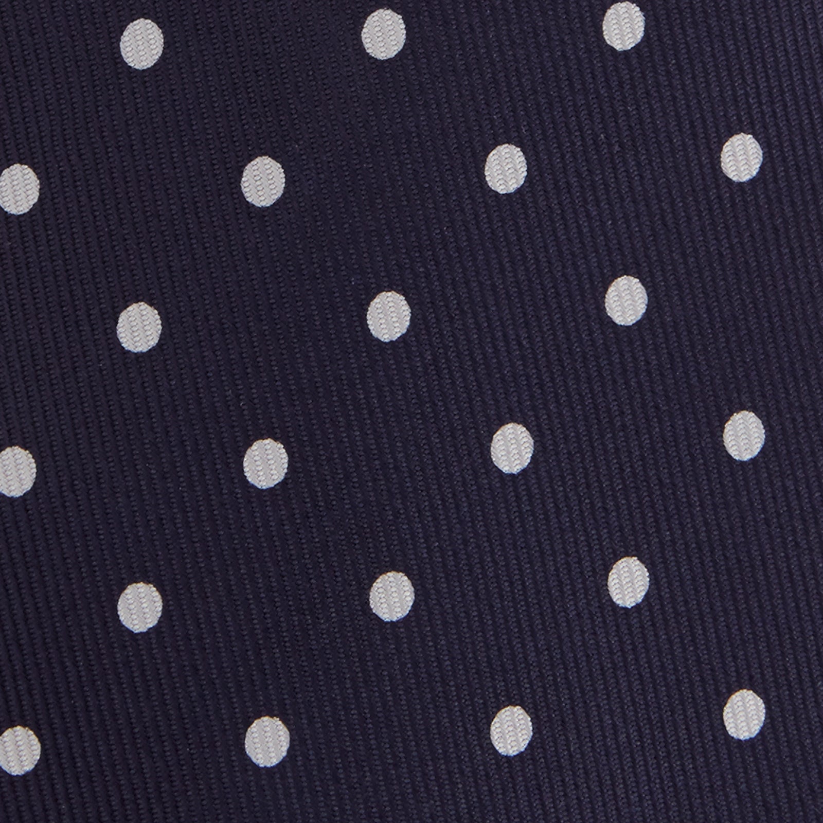 View 3 of product The Seven-Fold Navy Churchill Spot Silk Tie by Turnbull & Asser features evenly spaced white polka dots on navy silk—a luxury neckwear piece rolled up and displayed on a white background.