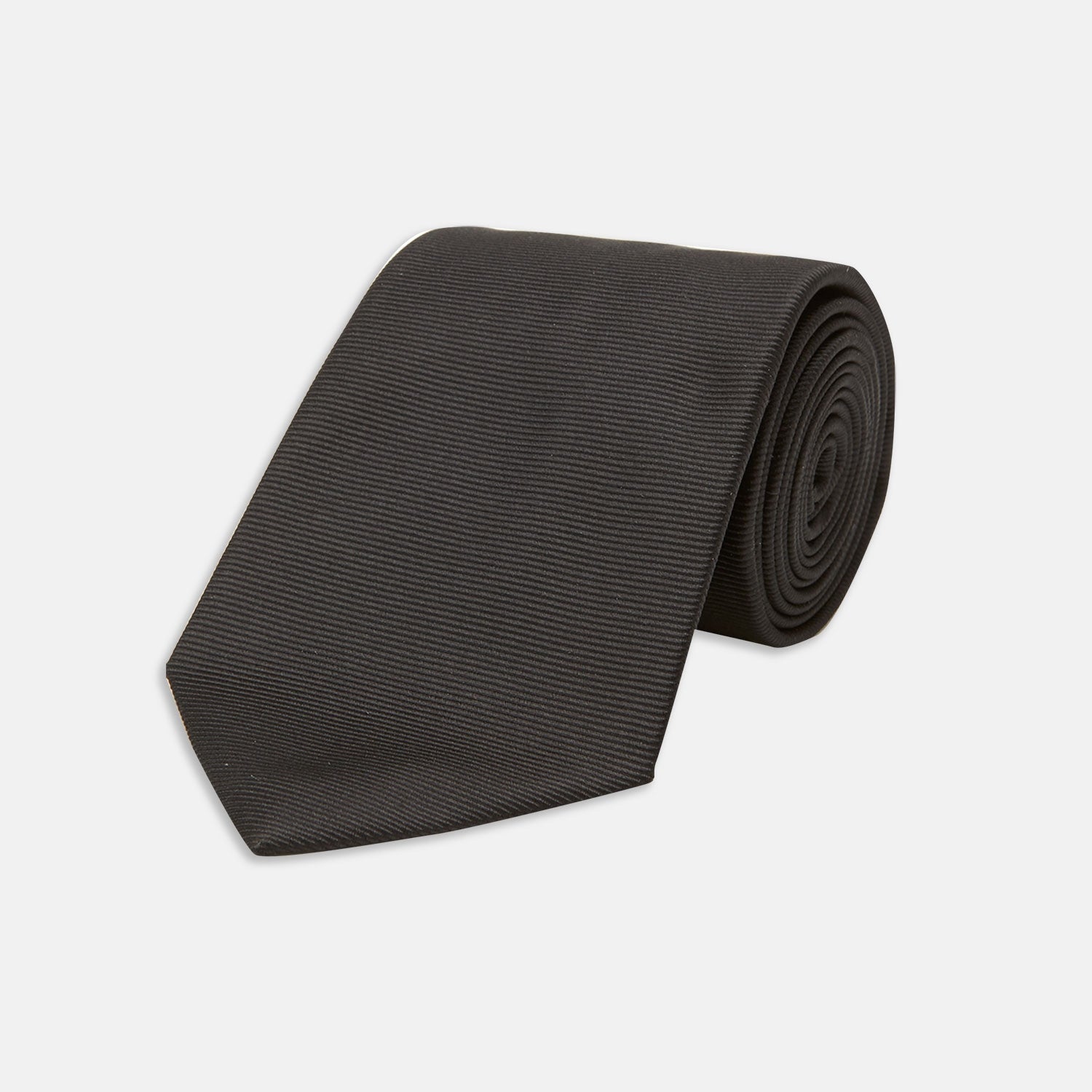 View 1 of product The Turnbull & Asser Slim Black Twill Silk Tie is neatly rolled on a white background, offering an ideal smart finish when paired with cotton shirts.