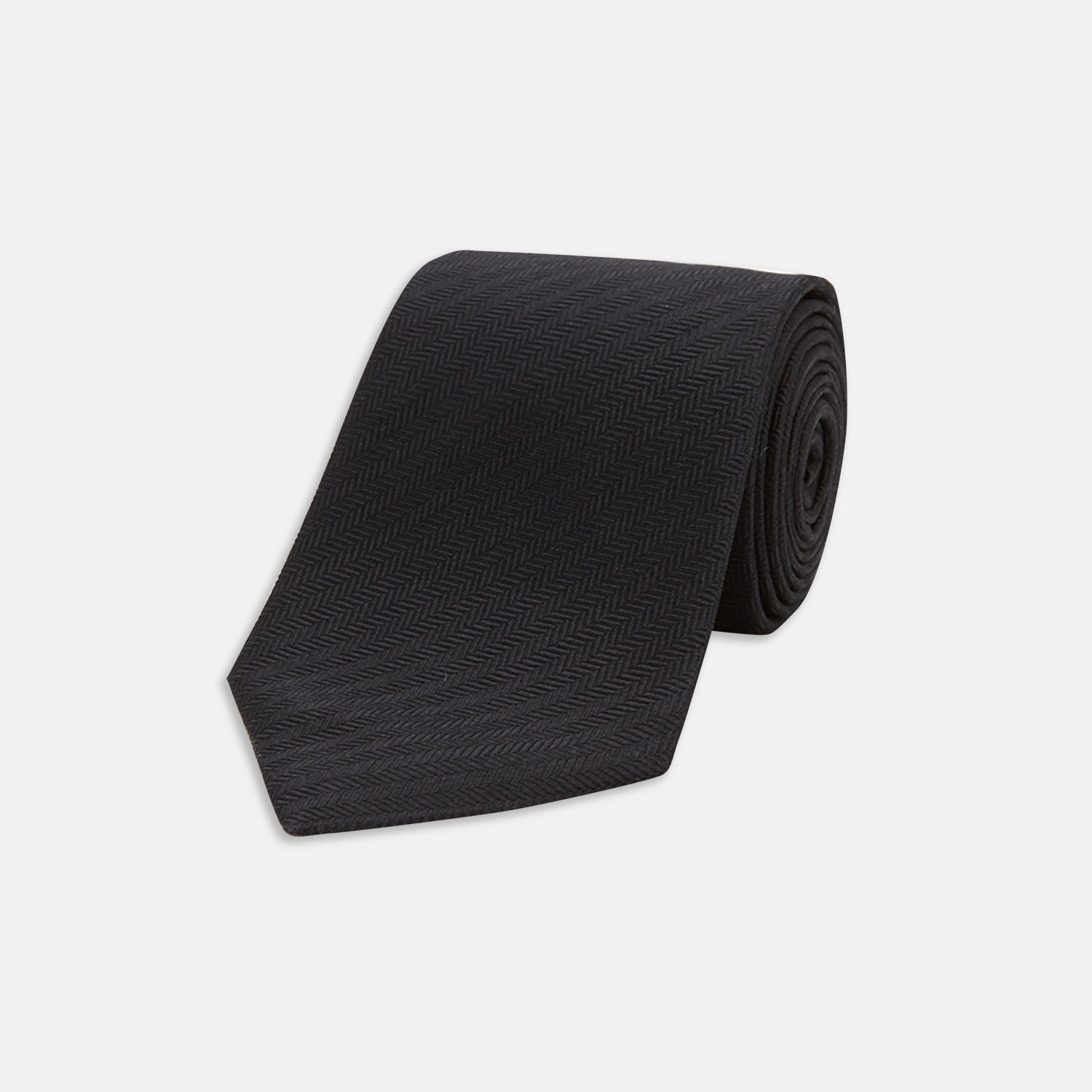 View 1 of product The Turnbull & Asser Slim Black Herringbone Silk Tie is neatly rolled, showcasing its subtle weave on a plain white background.