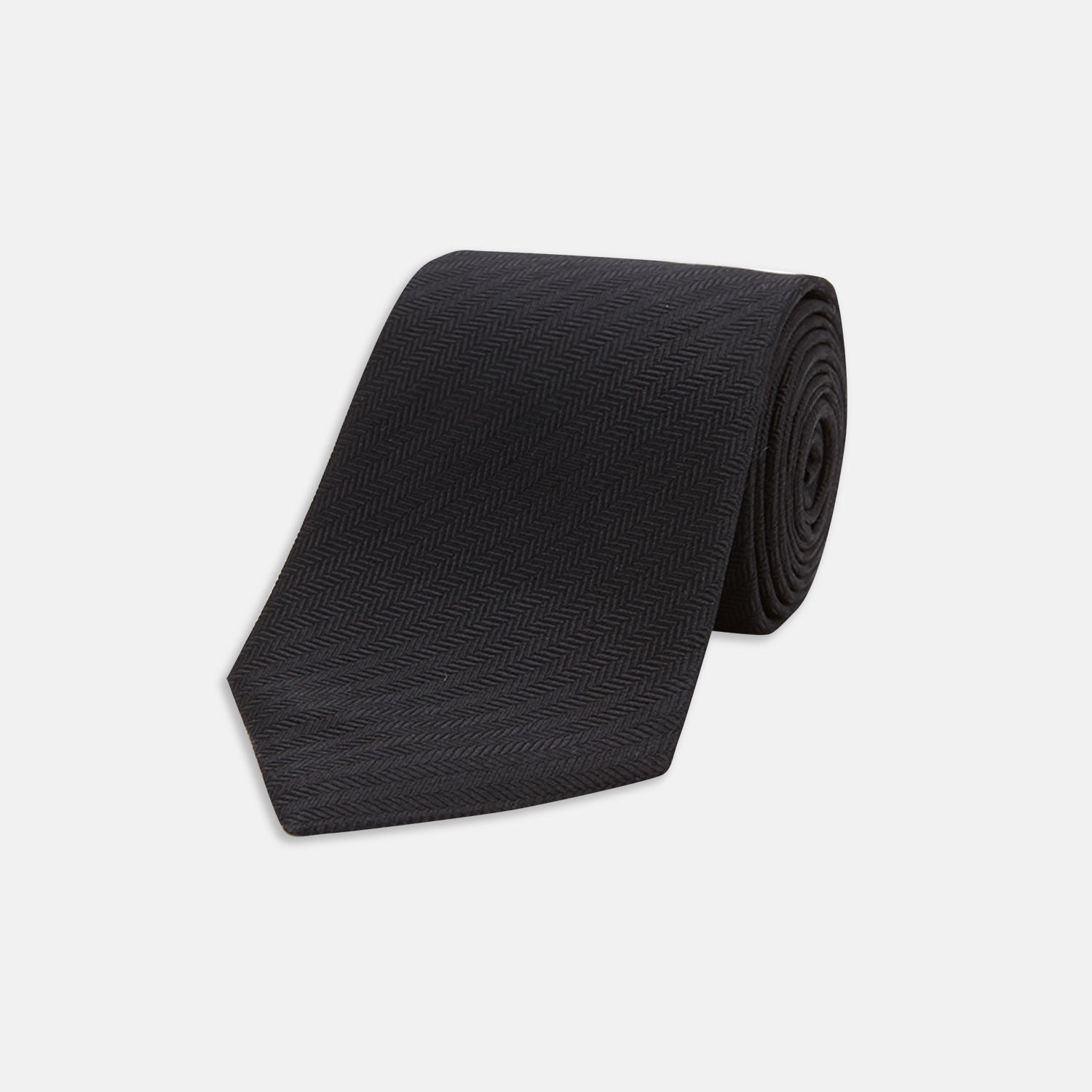 View 1 of product The Turnbull & Asser Black Herringbone Silk Tie is rolled up and displayed on a plain white background, showcasing its classic style and subtle chevron pattern.