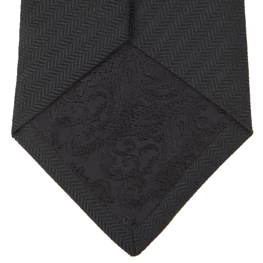 The Turnbull & Asser Slim Black Herringbone Silk Tie is neatly rolled, showcasing its subtle weave on a plain white background.