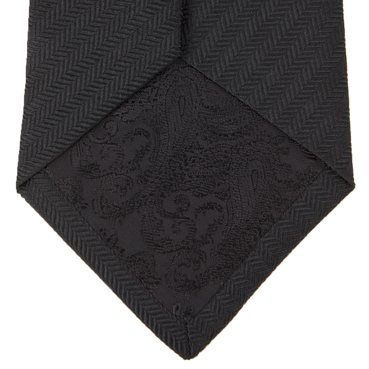 View 4 of product The Turnbull & Asser Black Herringbone Silk Tie is rolled up and displayed on a plain white background, showcasing its classic style and subtle chevron pattern.