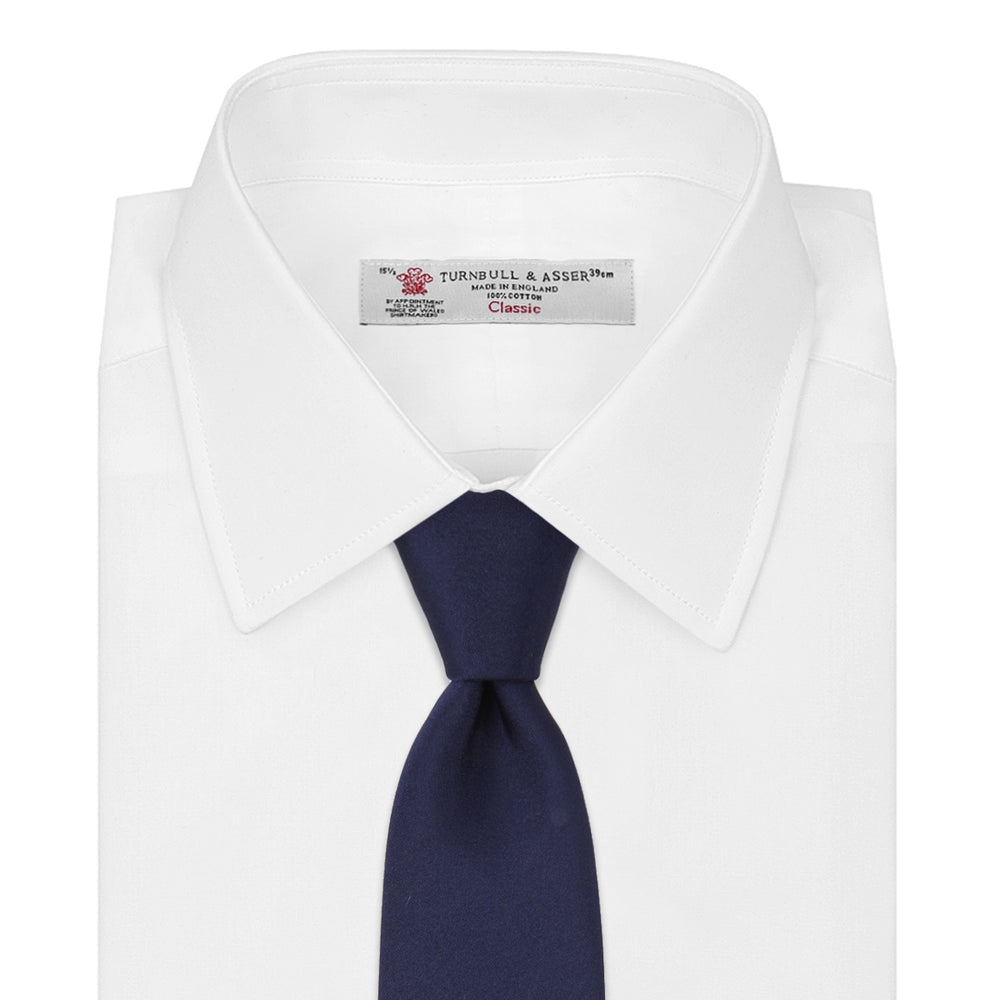The Turnbull & Asser Seven-Fold Navy Plain Satin Silk Tie is neatly rolled and showcased against a plain light gray background.