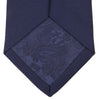 View 4 of product The Turnbull & Asser Seven-Fold Navy Plain Satin Silk Tie is neatly rolled and showcased against a plain light gray background.