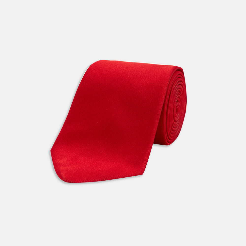 A Red Plain Satin Silk Tie by Turnbull & Asser is neatly rolled and displayed against a plain light gray background.