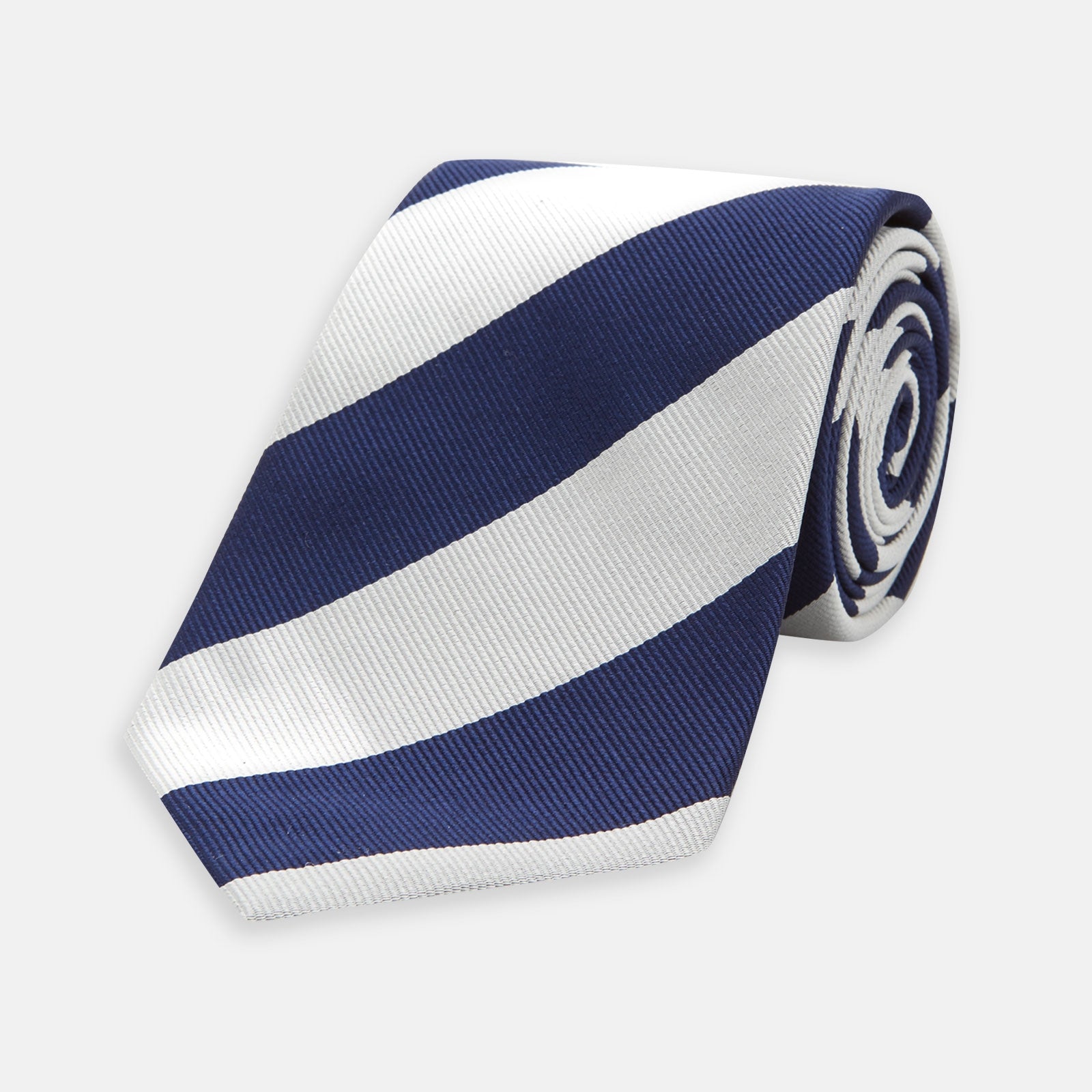 View 1 of product The Long Navy and Off-White Block Stripe Repp Silk Tie by Turnbull & Asser, featuring diagonal stripes, is rolled up and displayed on a plain white background—ideal for pairing with an office shirt.