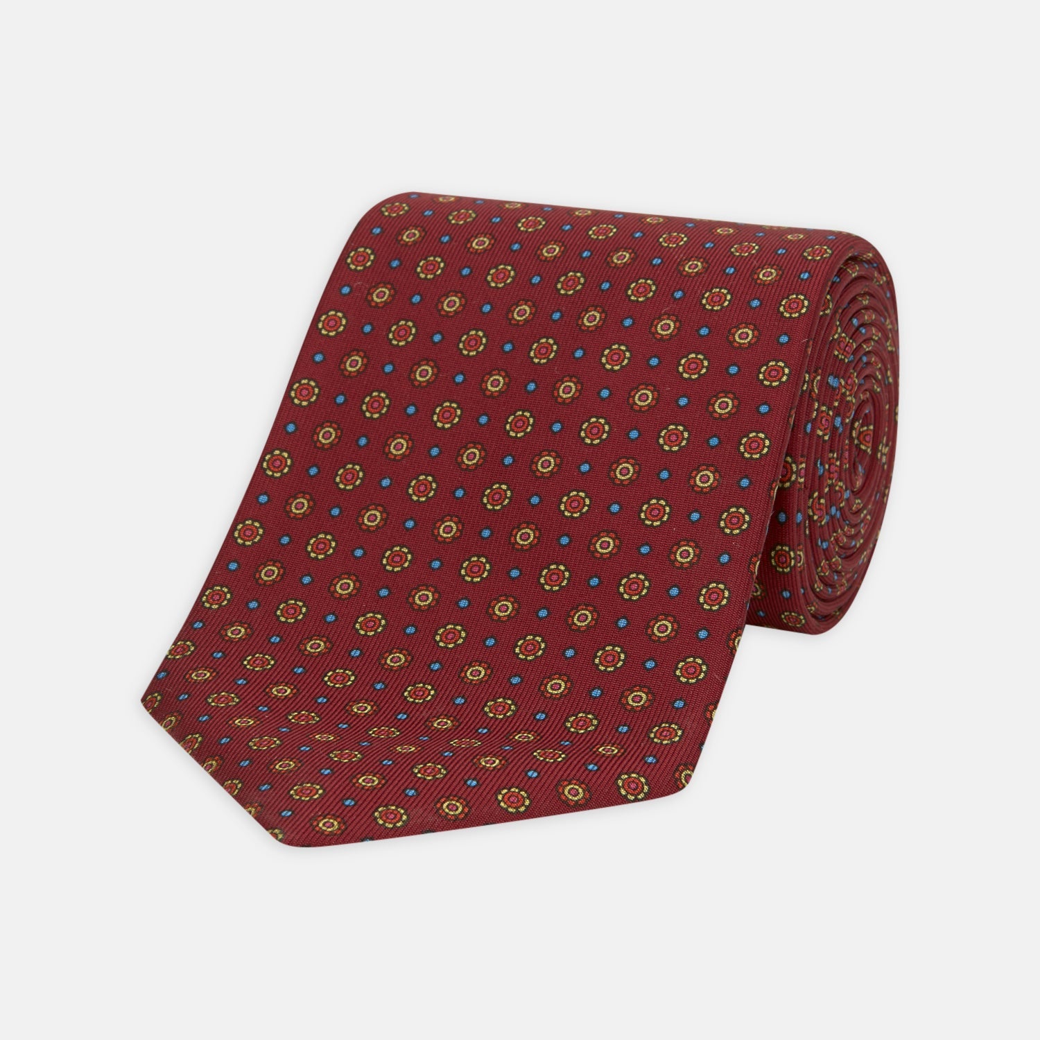 View 1 of product The Turnbull & Asser "The Great Gatsby" Burgundy Printed Silk Tie, from the Legends collection, showcases small circular floral motifs in yellow, blue, and green. Rolled with the tip forward, it is displayed against a white background.