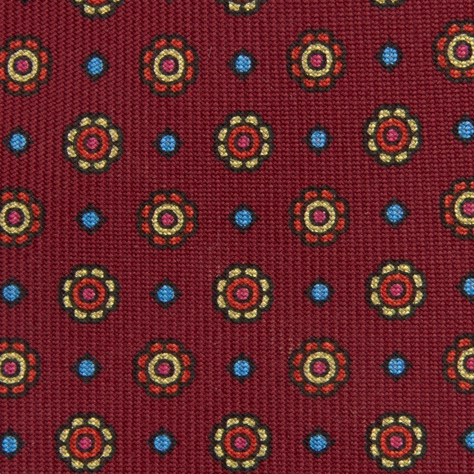 View 3 of product The Turnbull & Asser "The Great Gatsby" Burgundy Printed Silk Tie, from the Legends collection, showcases small circular floral motifs in yellow, blue, and green. Rolled with the tip forward, it is displayed against a white background.