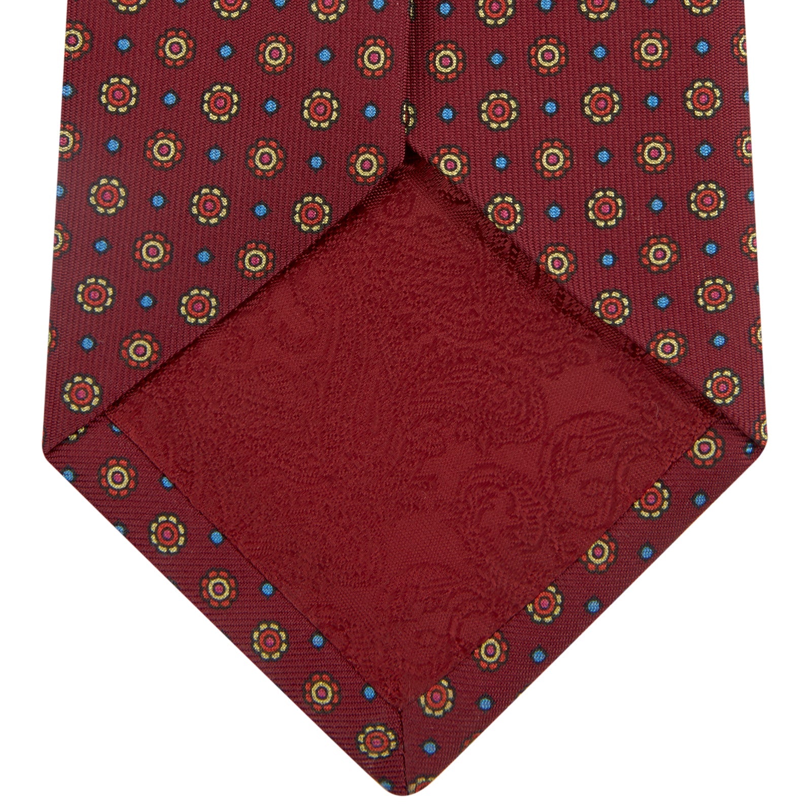 View 4 of product The Turnbull & Asser "The Great Gatsby" Burgundy Printed Silk Tie, from the Legends collection, showcases small circular floral motifs in yellow, blue, and green. Rolled with the tip forward, it is displayed against a white background.