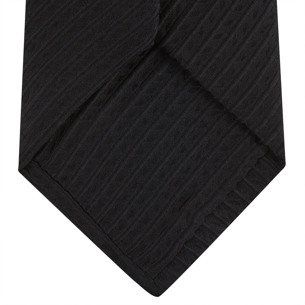 The Black Ottoman Silk Tie by Turnbull & Asser features a subtle wavy textured pattern and is crafted from heavyweight ribbed silk, shown rolled up against a plain white background.