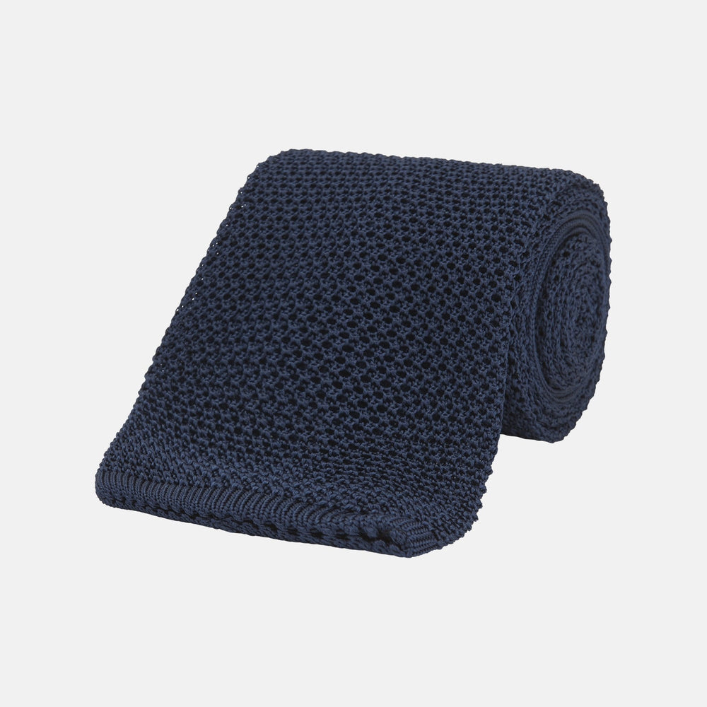 The Turnbull & Asser Navy Knitted Silk Tie features a textured open weave and flat squared ends, making it a versatile accessory for the modern gentleman’s wardrobe. Shown rolled up on a plain white background.