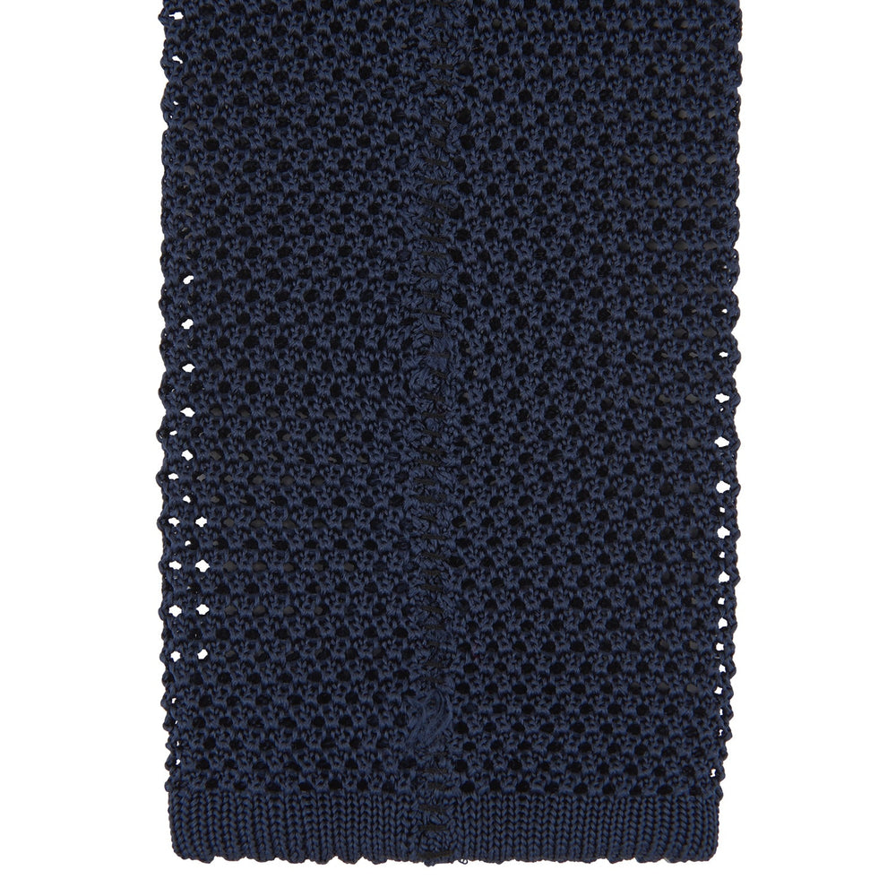 The Turnbull & Asser Navy Knitted Silk Tie features a textured open weave and flat squared ends, making it a versatile accessory for the modern gentleman’s wardrobe. Shown rolled up on a plain white background.