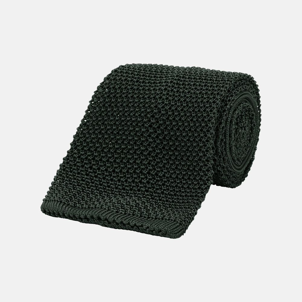 The Turnbull & Asser Green Knitted Silk Tie features a rich dark green hue and textured weave, making it an elegant accessory for any gentleman's wardrobe, shown rolled up against a light background.