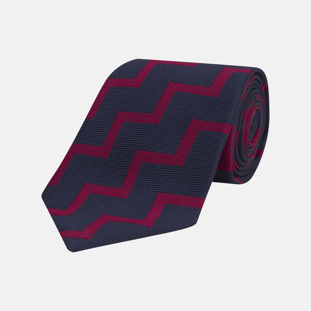 The Turnbull & Asser Navy and Red Striped Zigzag Silk Tie, featuring a striking pattern, is elegantly rolled on a white background—ideal for the modern gentleman.